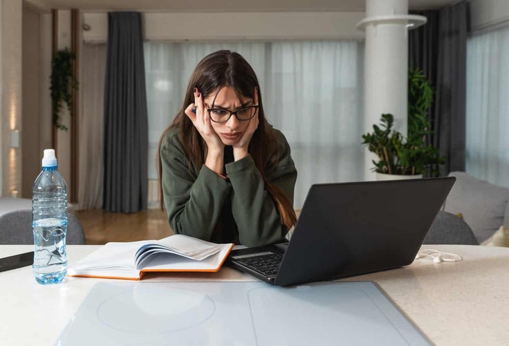 A woman sitting at her laptop, clearly frustrated about loading times.